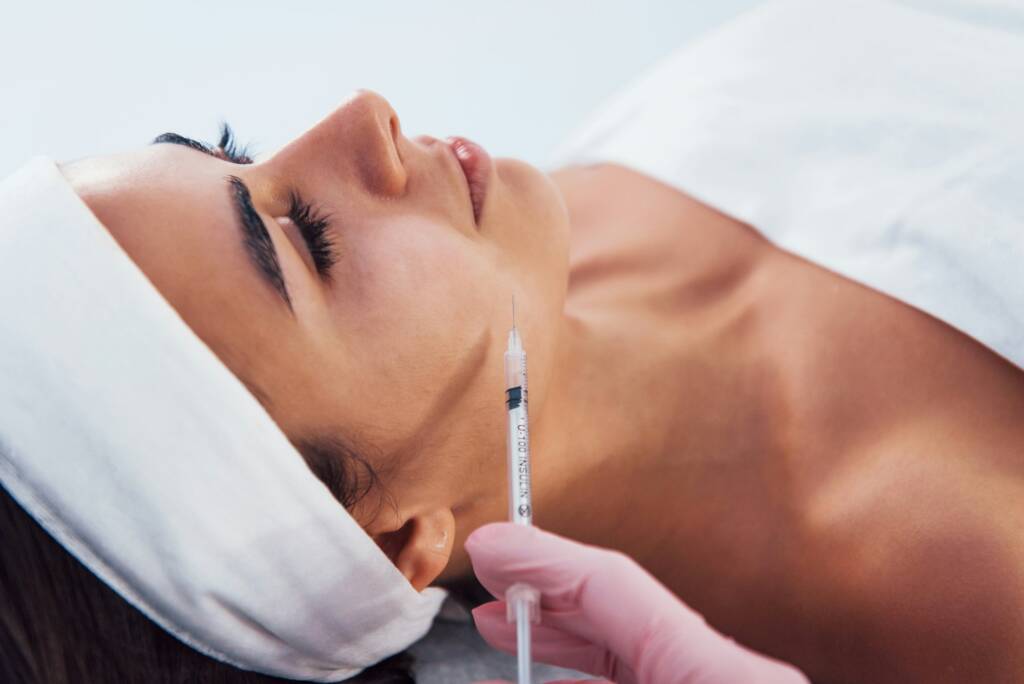 Woman that lying down in spa salon and have injection by the syringe into her face skin